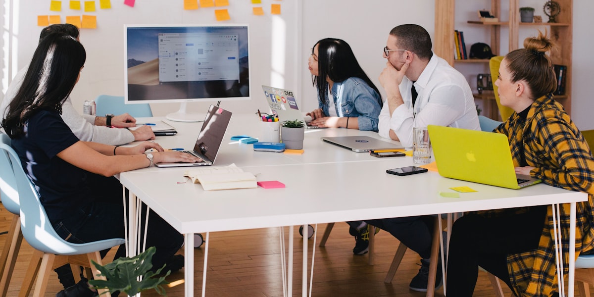 Team reviewing data on laptops and a wall monitor, representing AI hiring momentum and IT employer caution