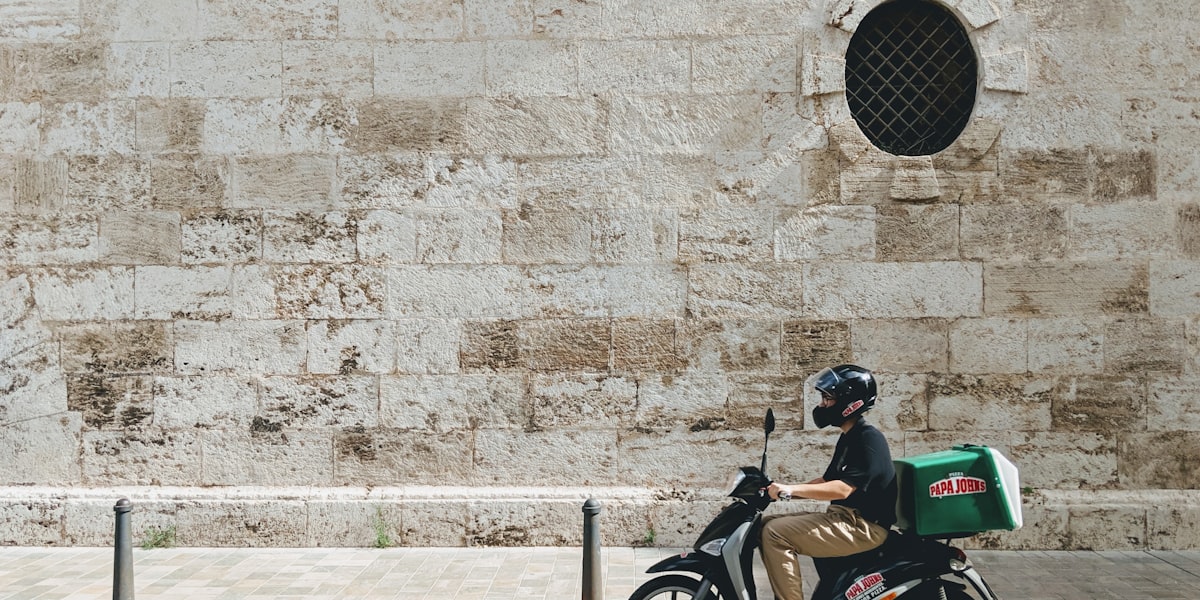Delivery rider on a scooter with a branded food-delivery box, representing platform and gig-based delivery work